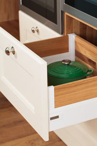 A wooden cabinet drawer with a polished handle and a green casserole dish