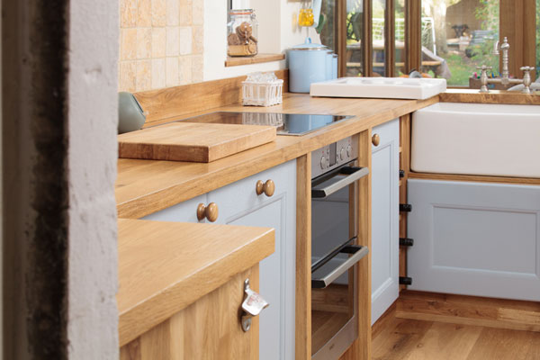 A kitchen with wooden worktop, blue cabinets and a stainless steel oven