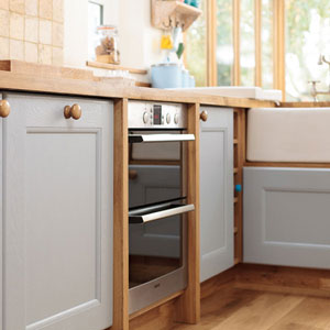 A kitchen with oak worktops, pale blue cabinets, a Belfast sink and a modern oven