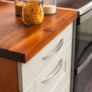 White cabinets are topped with a solid wood worktop. The cabinets have bow handles on.