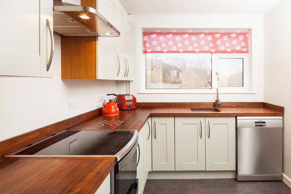 A neutral kitchen with stainless steel appliances and a red patterned window blind